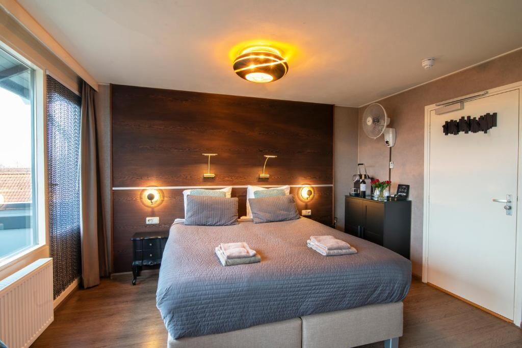 Camera d'albergo moderna con un letto grande, lampade ai comodini, una luce a soffitto, un ventilatore e vista sull'esterno.
