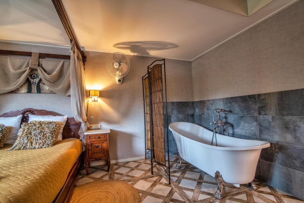 Un dormitorio con cama, mesita de noche, lámpara y un ventanal con cortinas.