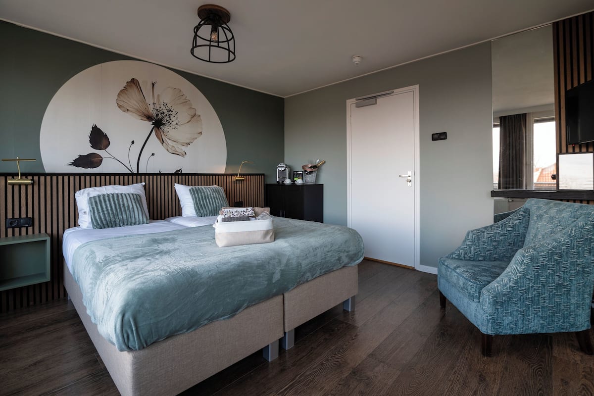 A bedroom with a bed, a chair, a dresser, a wall-mounted TV, and a large floral artwork.