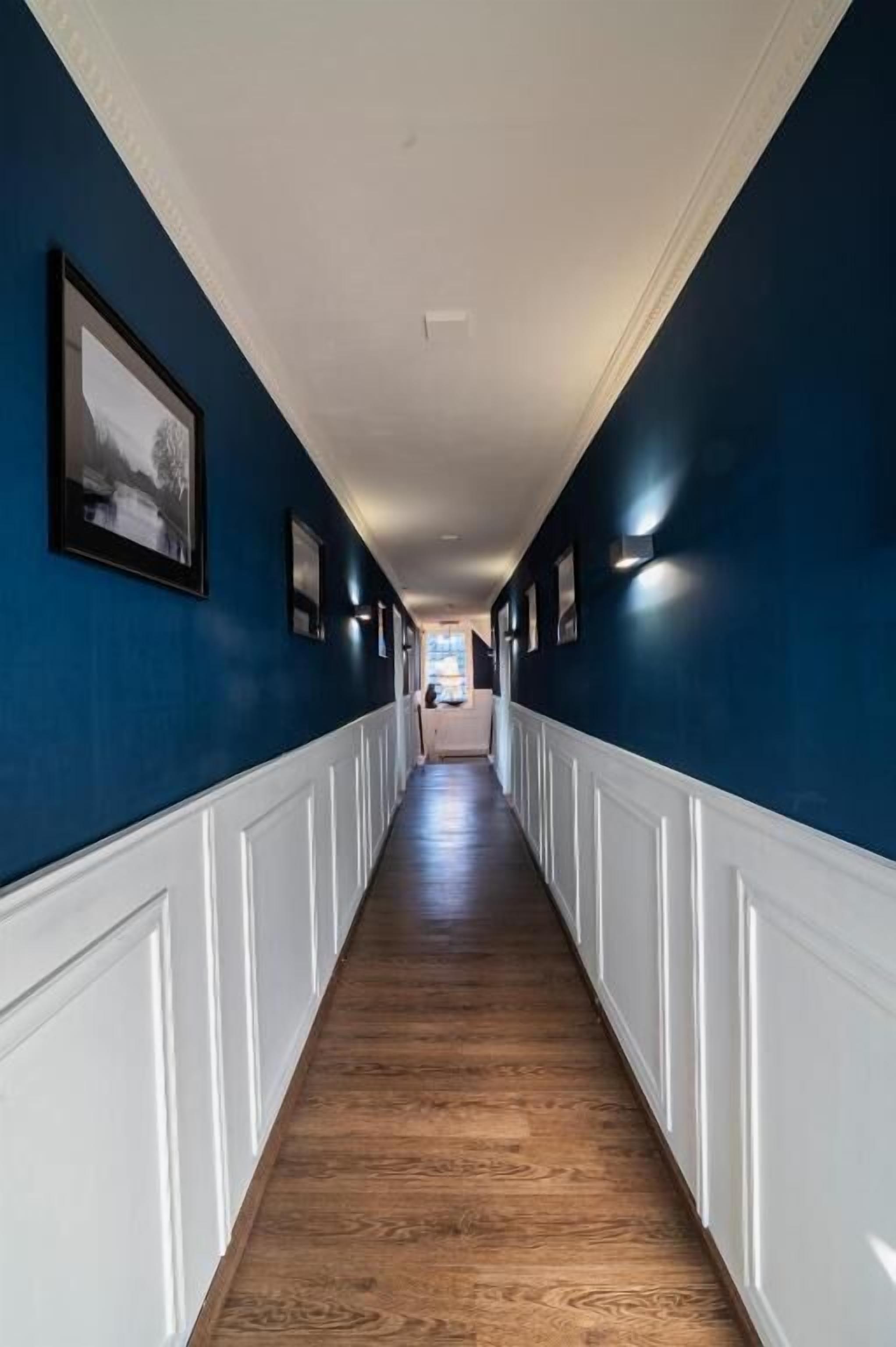 A long hallway with wooden flooring and white wainscoting, leading to a room at the end.