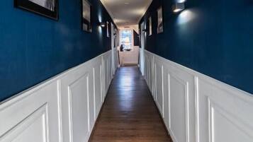 A long hallway with wooden flooring and white wainscoting, leading to a room at the end.