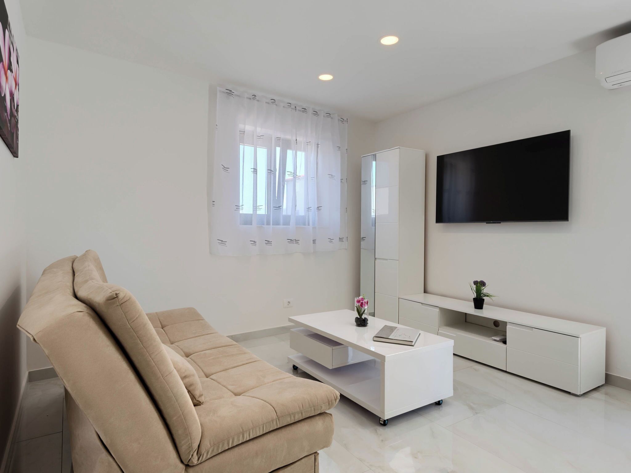 A modern living room with a sofa, a white TV stand, and a large mirror.