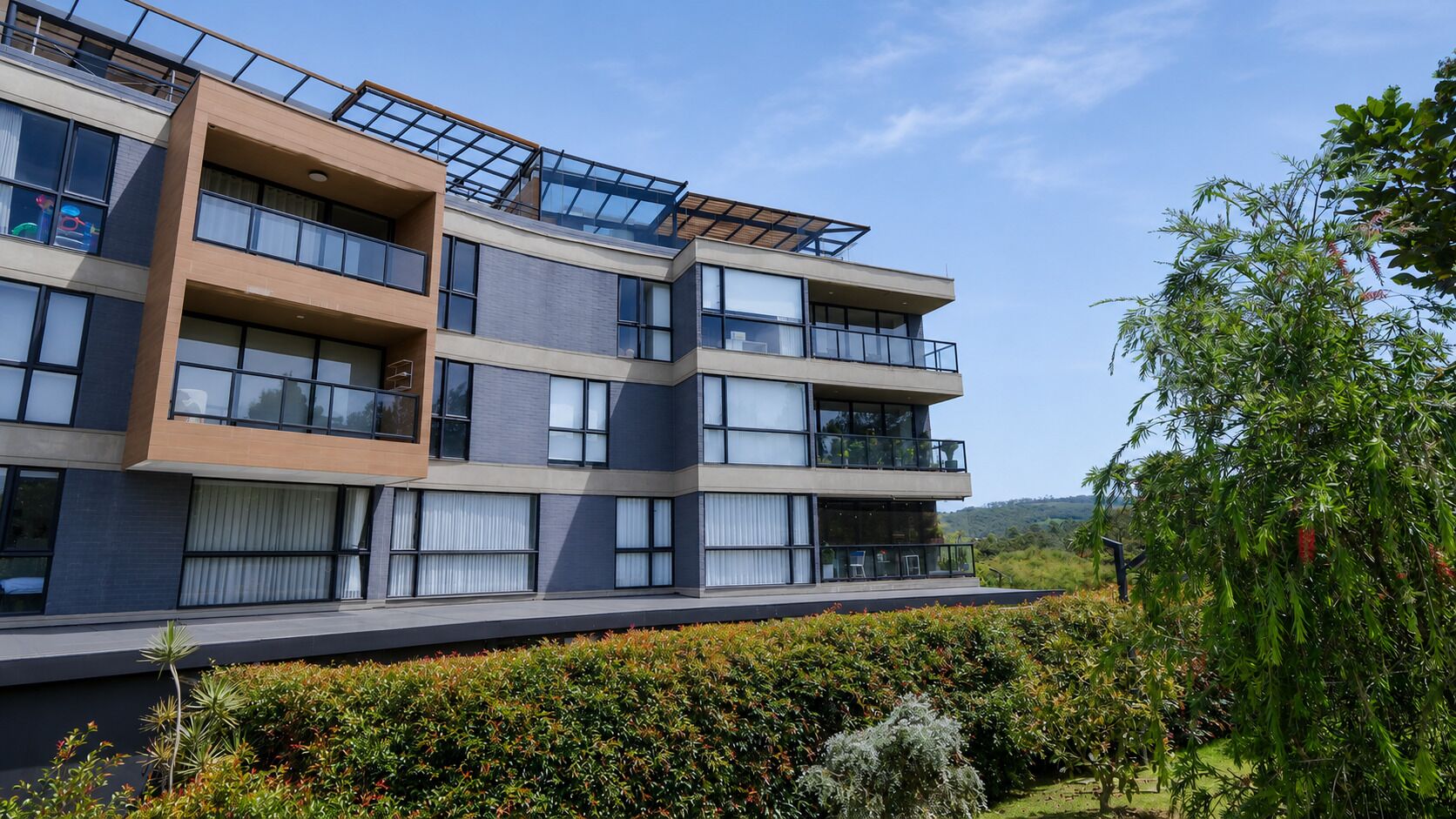 A multi-story residential building with balconies, large windows, and a landscaped garden.
