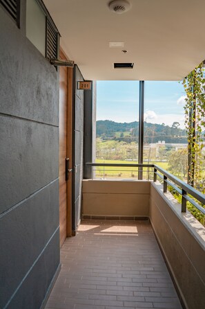 Un pasillo estrecho con una puerta que indica '201' da a un balcón con vistas a zonas verdes y colinas.
