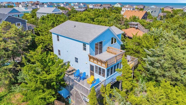 Et toetagers hus med balkon, omgivet af frodig vegetation og havudsigt.