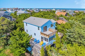 A two-story house with a balcony, surrounded by dense greenery and a view of the ocean. - Charming Oceanside Home in Avon with Sun Deck (Avon)