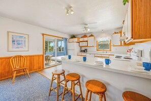 Una cocina con una isla central, sillas de madera, ventilador de techo y vistas a través de un ventanal.