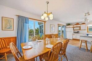 A dining room with a wooden table and chairs, a kitchen with a microwave, and a ceiling fan. - Charming Oceanside Home in Avon with Sun Deck (Avon)