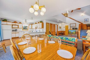A modern kitchen with white cabinets, a dining area with a wooden table set for six, and a living room with a sofa and TV. - Charming Oceanside Home in Avon with Sun Deck (Avon)