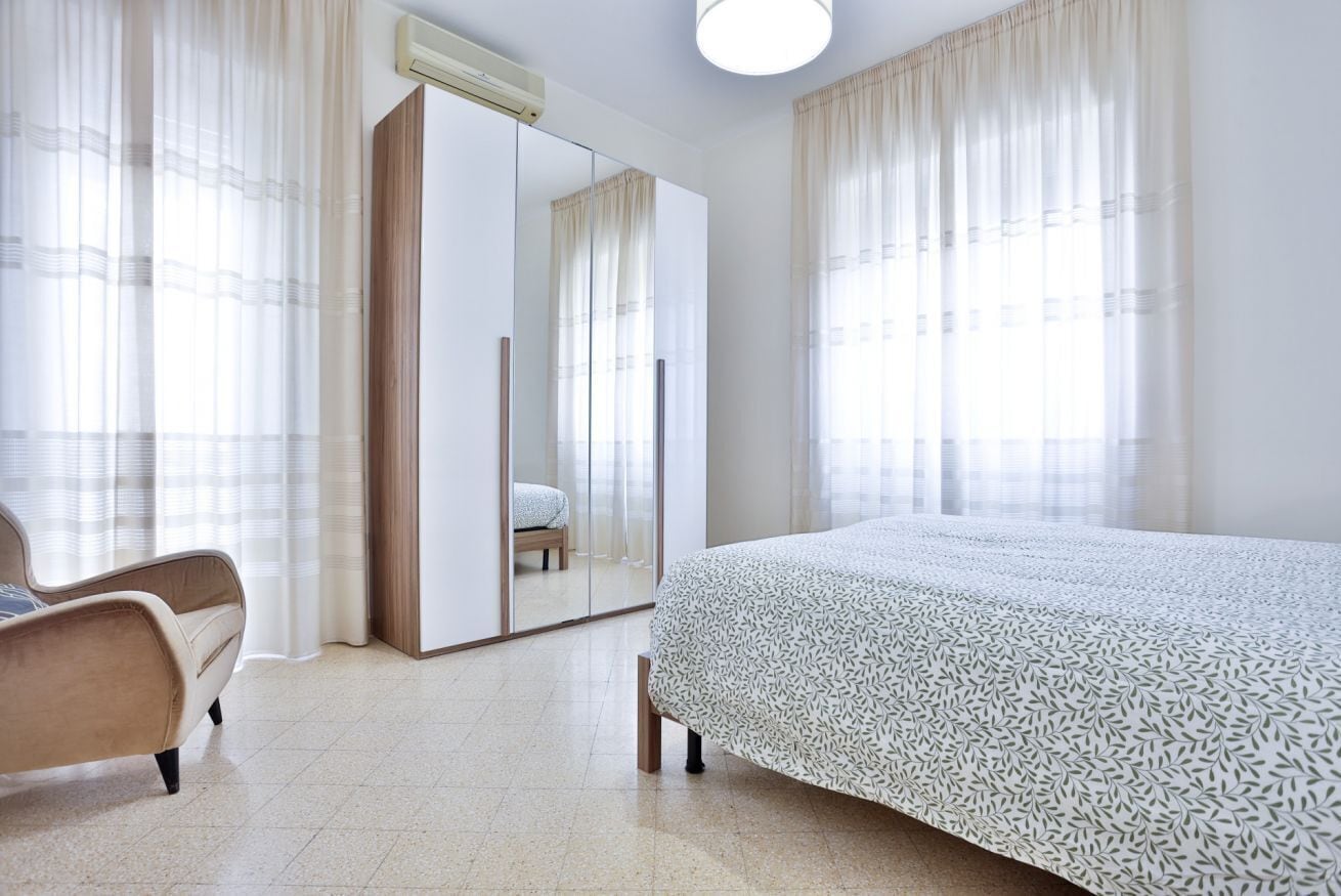 A bedroom with a bed, a chair, a wardrobe, and a mirror.