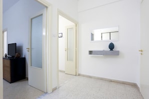 Ein Flur mit einer Tür, einem kleinen Schreibtisch mit Fernseher und einem an der Wand befestigten Regal mit Dekoration.