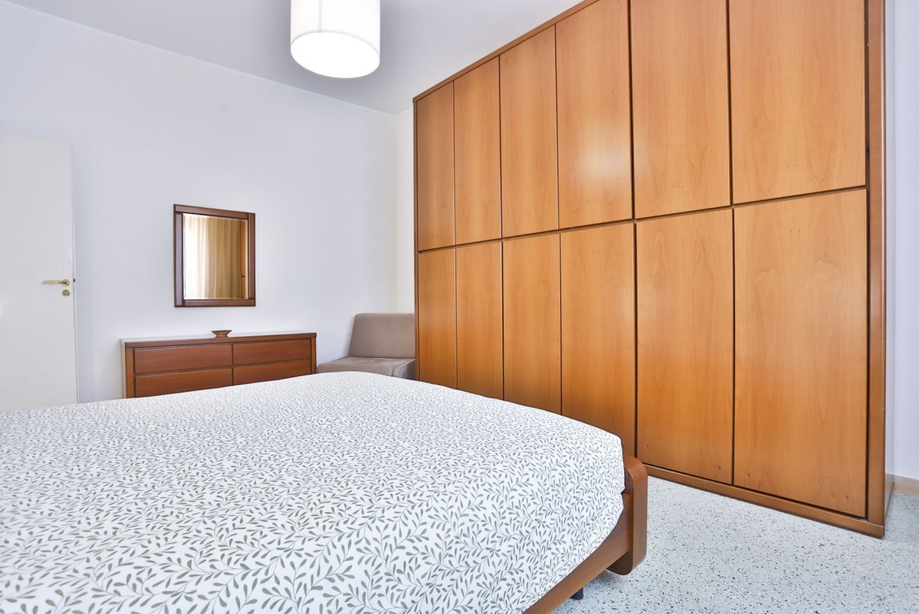 Ein Schlafzimmer mit einem Bett, einem Kleiderschrank, einem Schminktisch und einem Sessel.