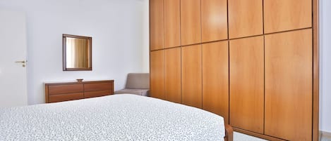 Un dormitorio con cama, armario, cómoda y una silla.