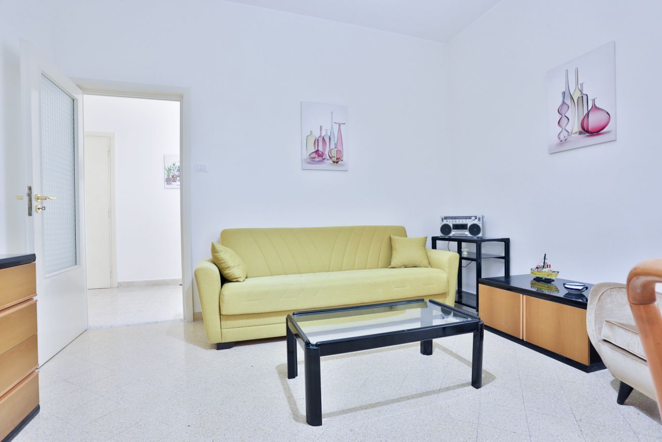 A living room with a yellow sofa, a glass coffee table, a radio, and artwork on the walls.