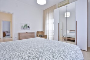 Ein Schlafzimmer mit einem großen Bett, einem Kleiderschrank, einem Sessel und einem Spiegel.
