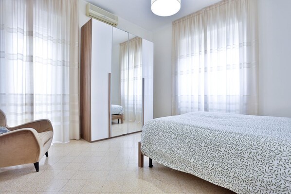 Ein Schlafzimmer mit Bett, Sessel, Kleiderschrank und Spiegel.
