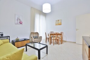 Ein modernes Wohnzimmer mit einer Couch, Couchtisch, Esstisch, Stühlen, einer Lampe und Kunstwerken an den Wänden.