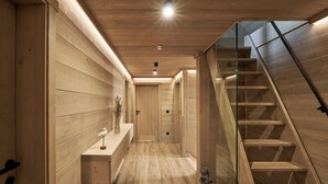 Een houten interieur met een trap, een bankje en een klein katbeeldje.