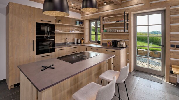 Een moderne keuken met houten kastjes, een centraal eiland, hangende lampen en uitzicht op de omgeving.