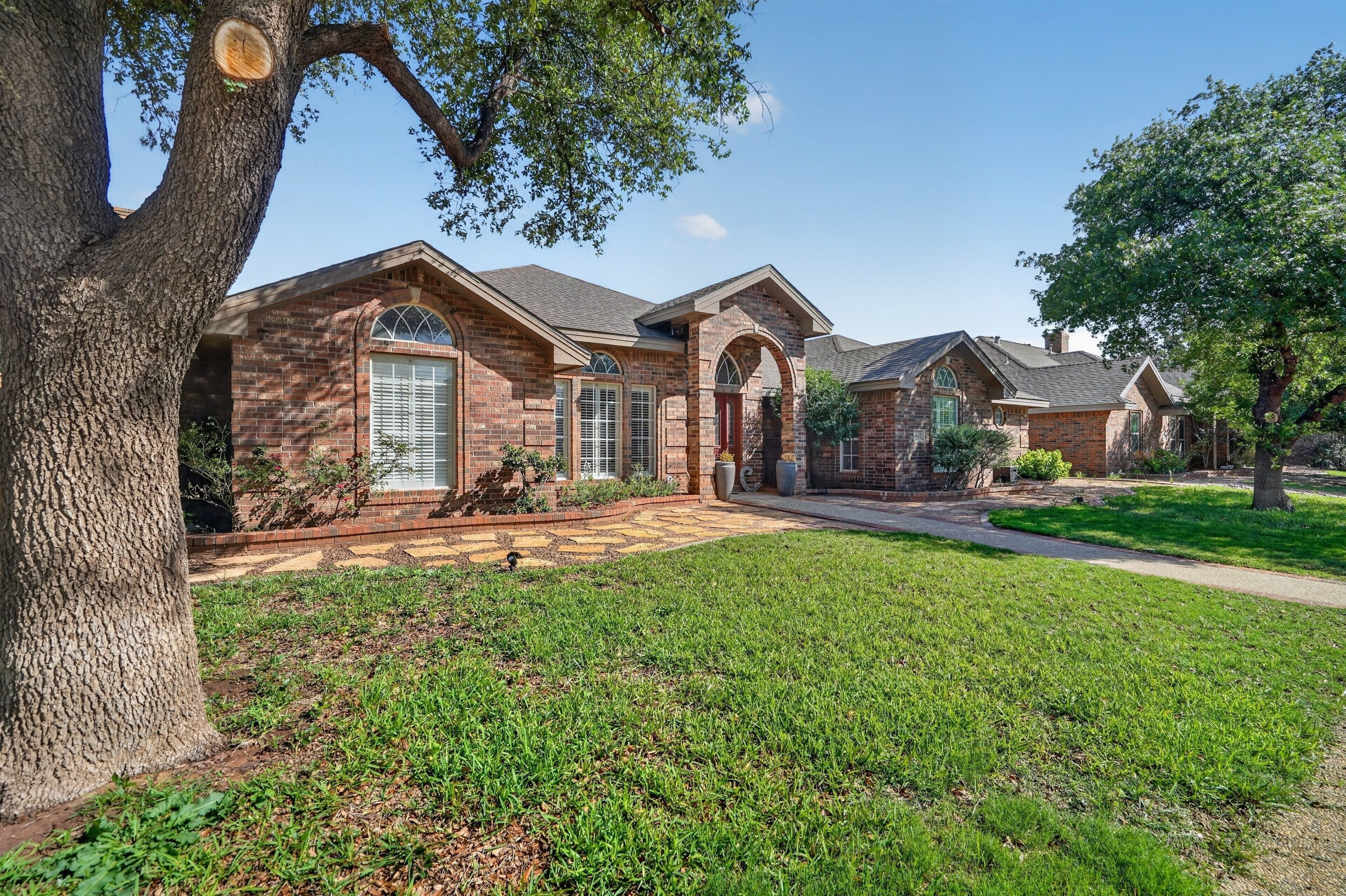 A brick house with a large lawn, a driveway, and a tree.
