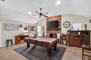 A spacious living room with a pool table, a fireplace, and a television mounted on the wall. - Roaring Fireplace Family Basecamp Midland Tx 4 Bedroom Home (Midland)
