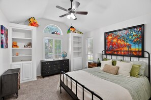 A bedroom with a bed, a ceiling fan, built-in shelving, a globe, and a painting. - Roaring Fireplace Family Basecamp Midland Tx 4 Bedroom Home (Midland)