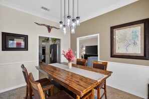 A dining area with a wooden table, chairs, a vase with flowers, a map on the wall, and a kitchen in the background. - Roaring Fireplace Family Basecamp Midland Tx 4 Bedroom Home (Midland)