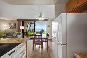 A kitchen with a view of the ocean, a dining area with chairs, a refrigerator, and a ceiling fan. - Kihei Beach, #108 1 Bedroom Condo (Kihei)