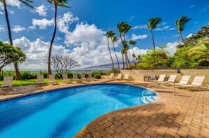 A swimming pool with lounge chairs and palm trees, surrounded by a brick patio. - Kihei Beach, #108 1 Bedroom Condo (Kihei)