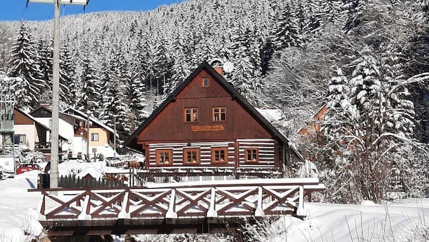 Una cabaña de madera con balcón, rodeada de árboles cubiertos de nieve y un cielo despejado.