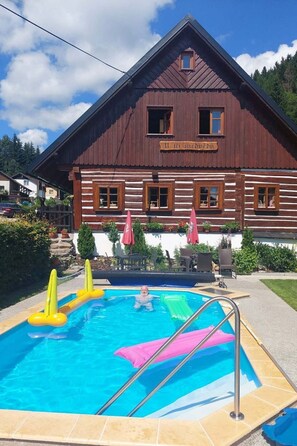 Ein Holzhaus mit Pool, einem Schild mit der Aufschrift 'Il tri medvedu' und Sitzgelegenheiten im Freien.