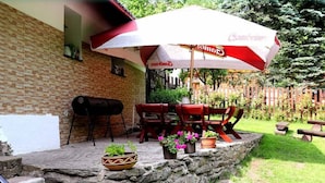 Un patio con muro de piedra, una parrilla, mobiliario exterior y un paraguas grande.