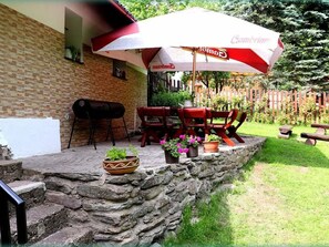 Eine Terrasse mit Steinmauer, Grill, Gartenmöbeln und einem großen Sonnenschirm.