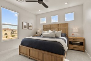 A bedroom with a large bed, a wooden headboard, bedside tables, a ceiling fan, and a view of the city. - Isle Stay Awhile 5 Bedroom Townhouse (Washington)