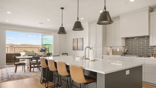 Une cuisine moderne dotée d’un grand îlot central, de luminaires suspendus et offrant une vue sur l’extérieur.