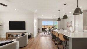 Une cuisine moderne avec un coin bar, un espace repas et un salon doté d’une grande télévision.