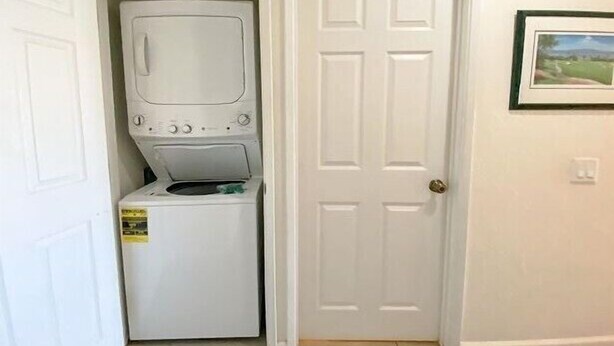 A laundry room with a washer and dryer, a door, and a framed picture on the wall. - Hale Kamaole 271- Paradise Found (Kihei)