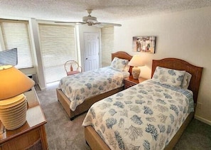 Ein Schlafzimmer mit zwei Betten, einem Deckenventilator, einer Tür und einer Lampe.