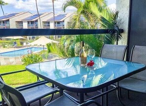 Ein Glastisch mit Stühlen, einer Flasche und einem Glas darauf, mit Blick auf einen Swimmingpool und Gebäude.