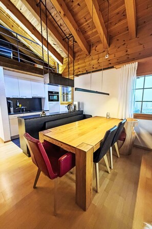 Eine moderne Küche mit Holztisch und Stühlen, einem Einbauofen und einem Fenster mit Vorhängen.