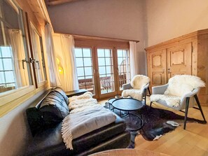 Ein gemütliches Wohnzimmer mit einer Ledersofa, zwei Sesseln, einem Couchtisch und einem großen Fenster mit Vorhängen.