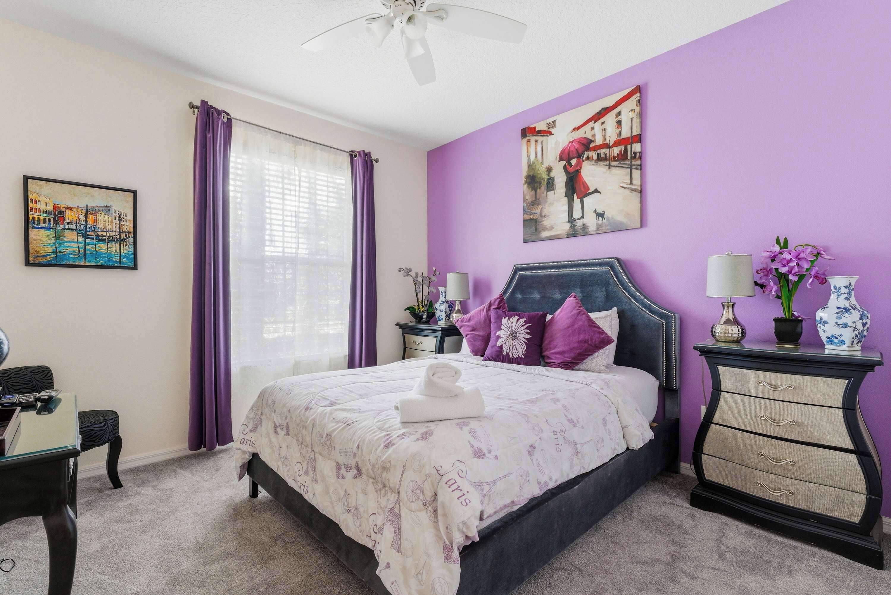 A bedroom with a bed, a nightstand, a dresser, a desk, and a window with curtains.