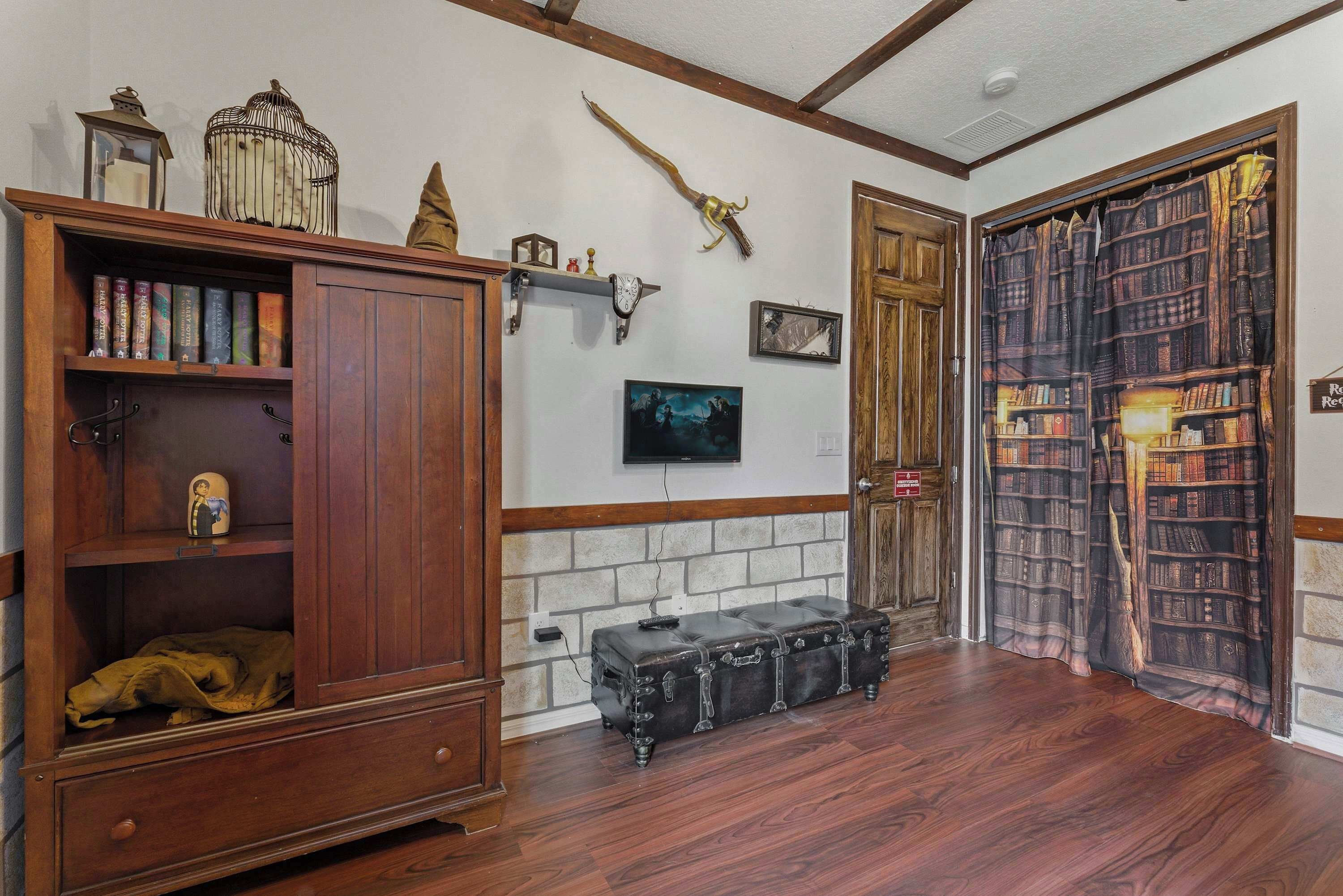 A room with a wooden cabinet, a leather trunk, a bookshelf, a mounted picture, and a door with a bookshelf curtain.