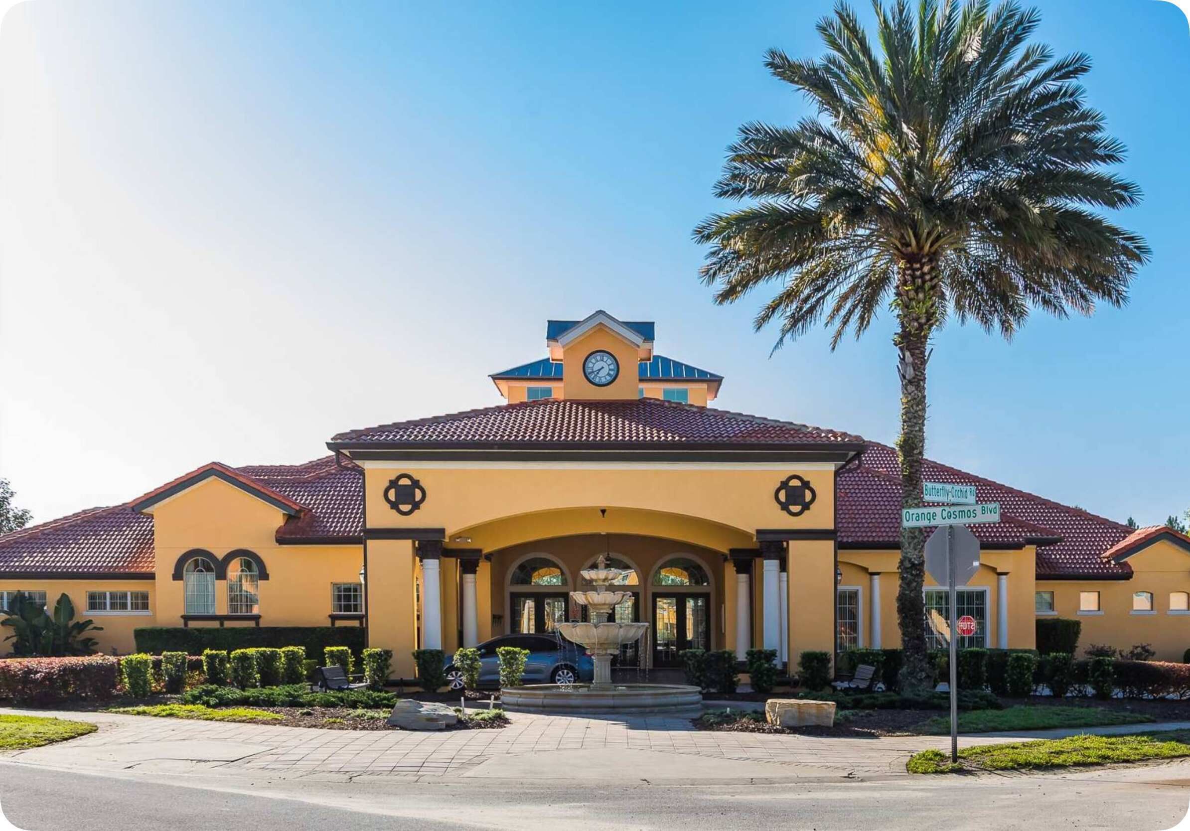 A large, yellow building with a clock tower, a fountain, and a palm tree in the foreground.