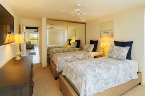 A hotel room with two beds, a ceiling fan, a desk with a lamp, and a painting on the wall. - Island Retreat - Two bedroom Two bathroom Hale Kamaole 329 (Kihei)