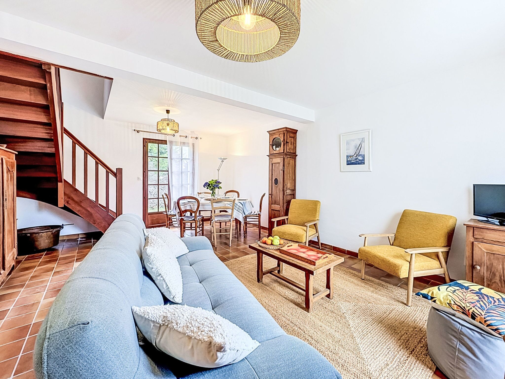 Una sala de estar con sofá, sillas, una mesa de centro, televisión, escalera y un comedor.