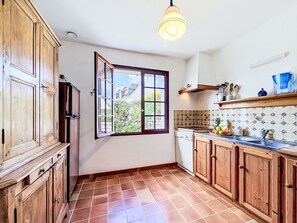 A kitchen with wooden cabinets, a window, a tiled backsplash, and a hanging light fixture. - La littorine by Interhome (Quiberon)