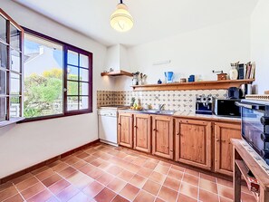 Una cucina con mobili in legno, un frigorifero bianco, piastrelle a parete e una finestra che si affaccia sul verde.