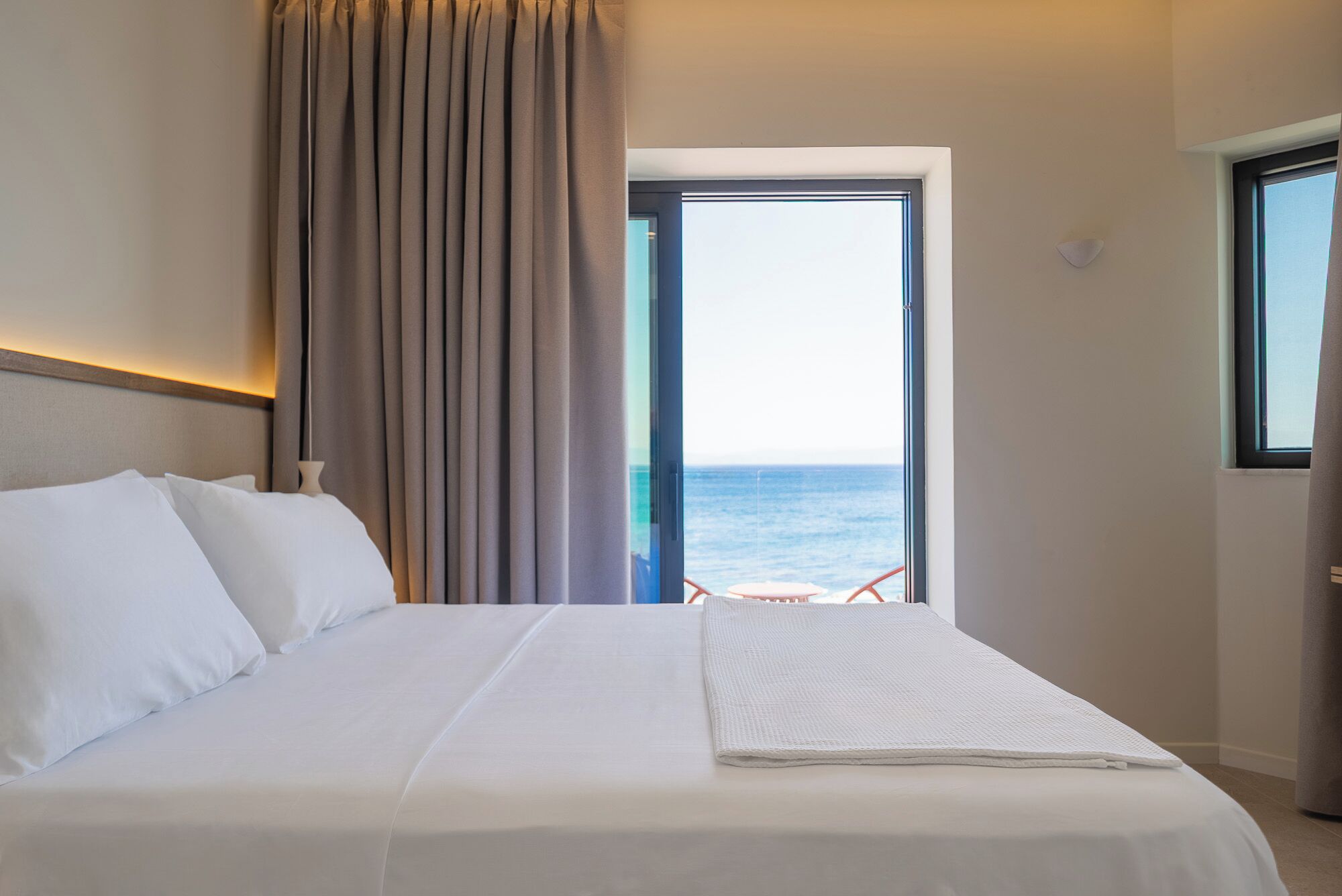 A hotel room with a bed, a view of the sea, and a balcony.