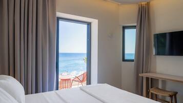 Ein Hotelzimmer mit Bett, Fernseher, kleinem Tisch, Korbsessel und einem Balkon mit Meerblick.